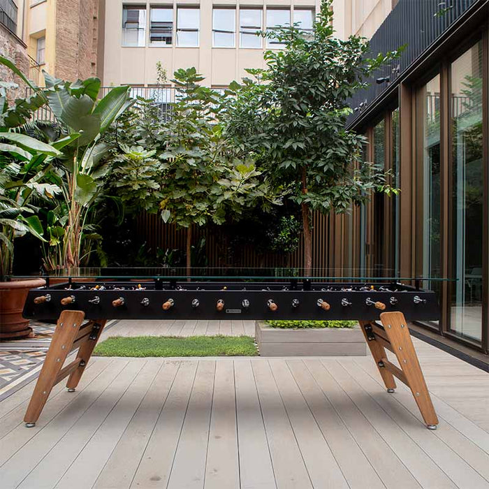 RS Barcelona RS MAX outdoor dining football table with glass top and wooden legs positioned in a modern garden patio setting.