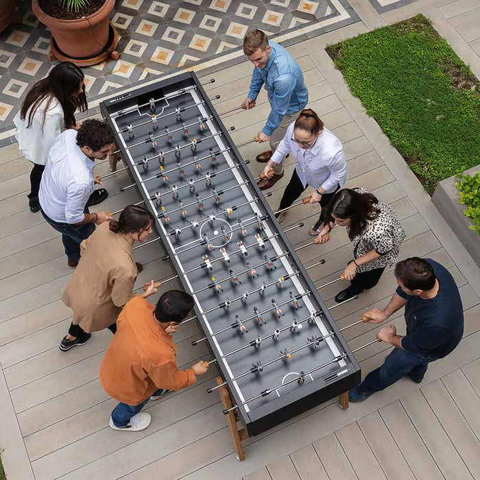 Group of people playing on the RS Barcelona RS MAX football table, a large social foosball table designed for multiple players in outdoor entertainment spaces.