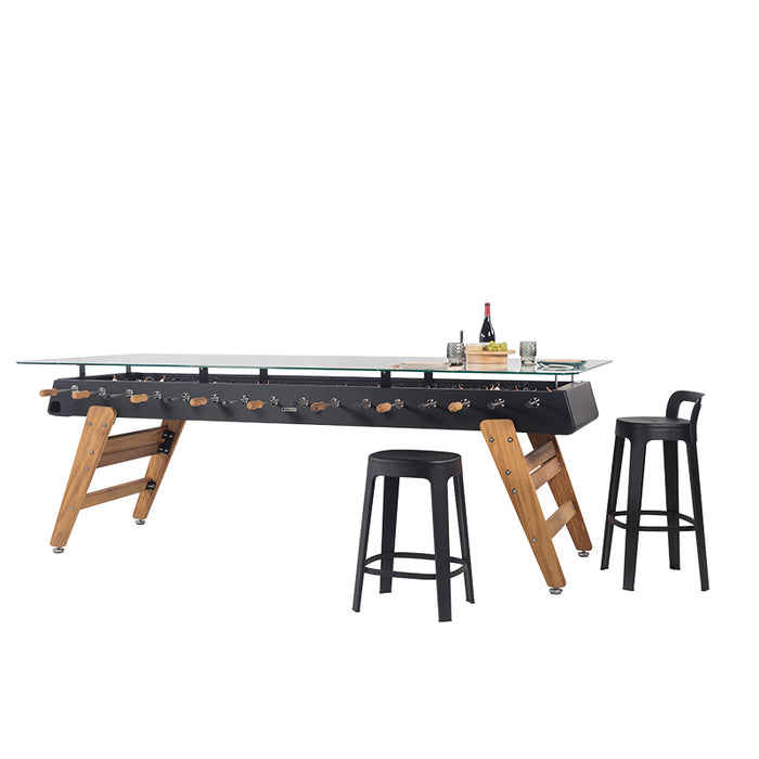 Angled view of RS Barcelona RS MAX glass top dining football table with stools showing the integrated foosball game beneath.