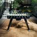 Black RS Barcelona RS2 dining football table with glass top placed on a stylish patio, luxury outdoor foosball dining table surrounded by plants and modern architecture.