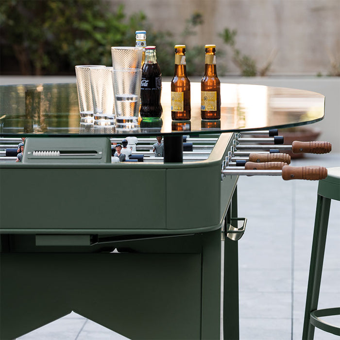 Outdoor RS Barcelona RS2 dining football table in green with glass top, featuring foosball players beneath and drinks on top, stylish multifunctional garden dining and gaming table.