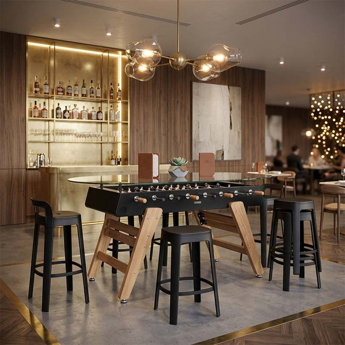 RS Barcelona RS3 dining football table with glass tabletop styled in a modern bar interior with stools, combining foosball table gameplay with contemporary dining furniture.