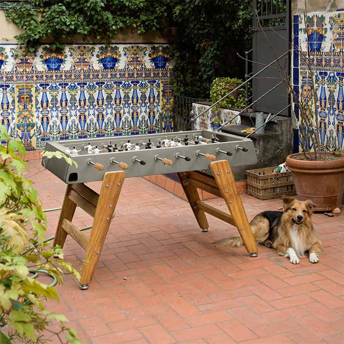 RS Barcelona RS3 Wood football table in rustic garden patio with decorative tiles and greenery, stylish outdoor foosball table with wooden legs and contemporary design.