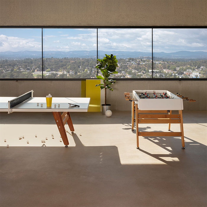 RS Barcelona RS3 Wood football table alongside table tennis table in spacious interior with large windows, modern recreational furniture with wooden legs and clean design