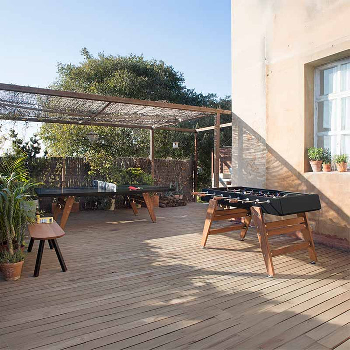 RS Barcelona RS3 Wood football table on outdoor wooden deck with table tennis setup, black frame and wooden legs, versatile outdoor gaming furniture in natural setting.