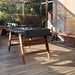 RS Barcelona RS3 Wood football table in sunlit outdoor terrace with wooden flooring and pergola, black foosball table with wooden legs in relaxed garden setting.