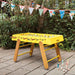 RS Barcelona RS4 Home football table in yellow with wooden legs placed outdoors in a garden setting, modern designer foosball table.