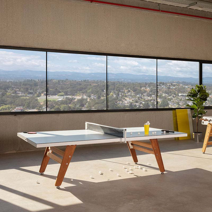 Modern RS Barcelona stationary ping pong table with grey top and wooden legs in a bright loft space with panoramic windows and scenic views.