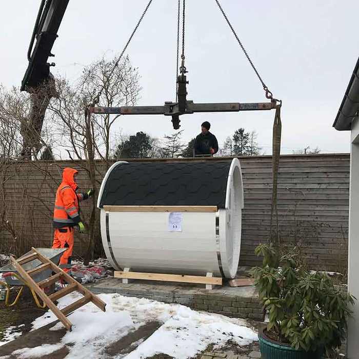 Two people installing the Sauna Barrel from Thermowood 1.9 x 2m in a garden.