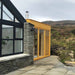 Traditonal Sauna Cube beside of modern house and surrounded by natural terrain with grass and rocks.