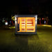 Saunum AirCube Space Outdoor Sauna illuminated in a lush garden setting at night, with warm lighting glowing through the large glass panels.