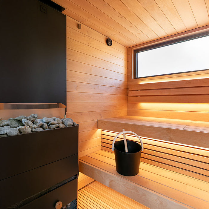 The interior of the Saunum AirCube Terrace Outdoor Sauna featuring a modern black heater, wooden benches, and a sauna bucket, creating a clean and relaxing atmosphere.