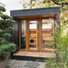 The Saunum AirCube Terrace Outdoor Sauna positioned on a garden patio, featuring a modern black exterior and large glass doors, with natural greenery surrounding the area for a peaceful outdoor retreat.