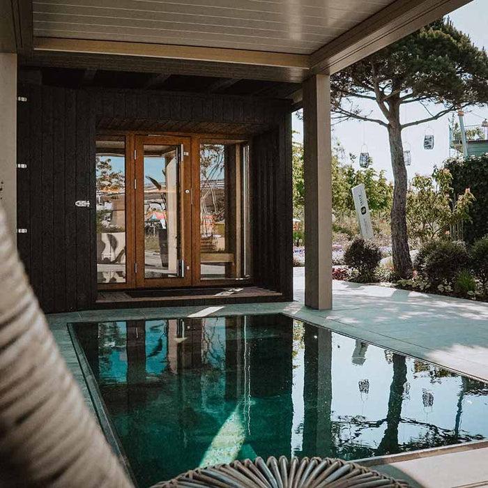 The Saunum AirCube Terrace Outdoor Sauna, positioned beside a pool on a modern patio, featuring a sleek black design and large windows.