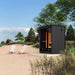 The Saunum Classic Mini-Mini Outdoor Sauna set in a serene beachside location, featuring a sleek black Thermo-Spruce exterior and large glass panels. This 2-3 person sauna offers a luxurious and compact wellness retreat, perfect for blending relaxation with nature.