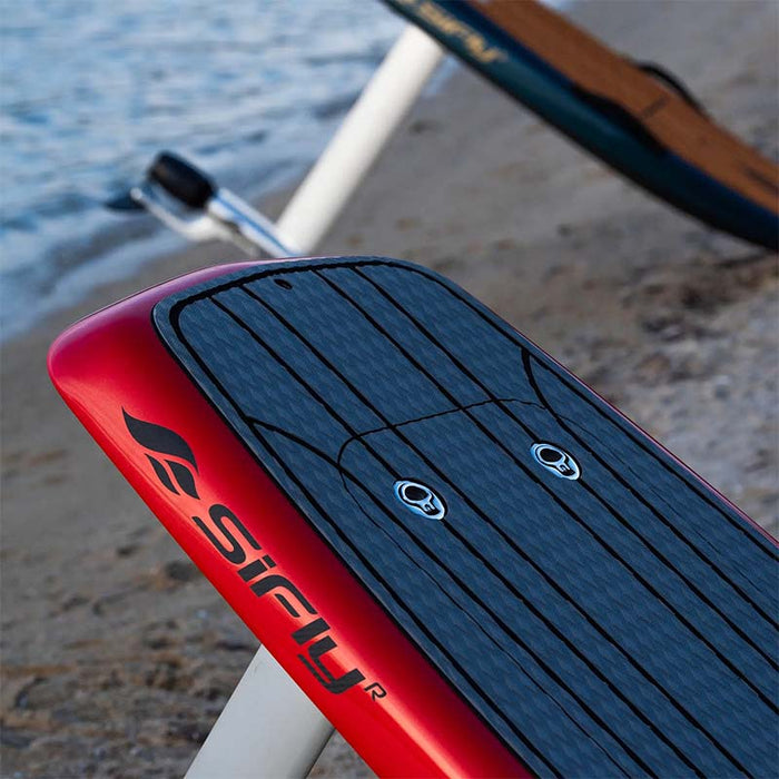 Close-up of the red SiFly Stellar eFoil board with textured deck pad and branded side rail by the water.