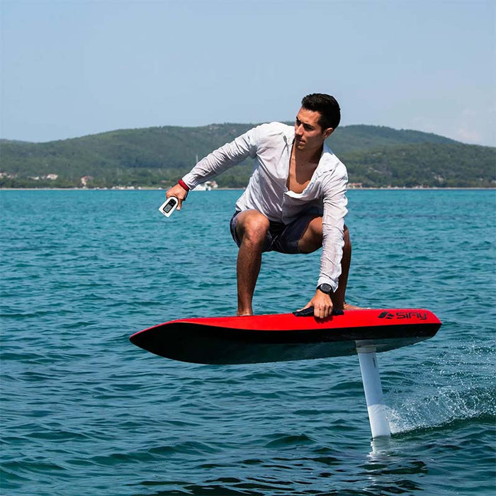Rider crouching on a red SiFly Stellar eFoil board while hydrofoiling above turquoise sea water.