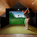 Golfer mid-backswing on the Simbooth 1 Golf Simulator Kit in a warm-toned attic space, offering precise indoor golf training and high-resolution screen projection.