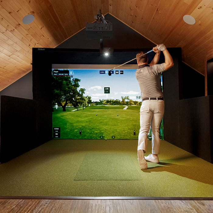 Man finishing a swing on the Simbooth 1 Golf Simulator Kit under a sloped wooden ceiling, demonstrating realistic virtual course play and space-efficient installation.