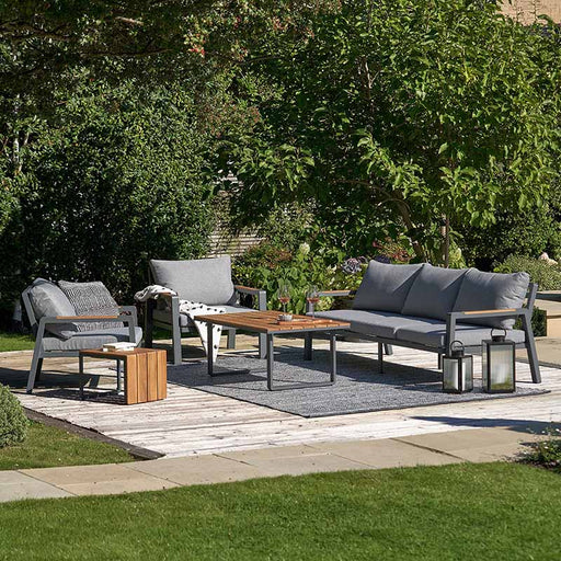 Stockholm Outdoor Seating Set in a garden setting, featuring an anthracite frame with natural teak accents and comfortable grey cushions, perfect for outdoor relaxation.