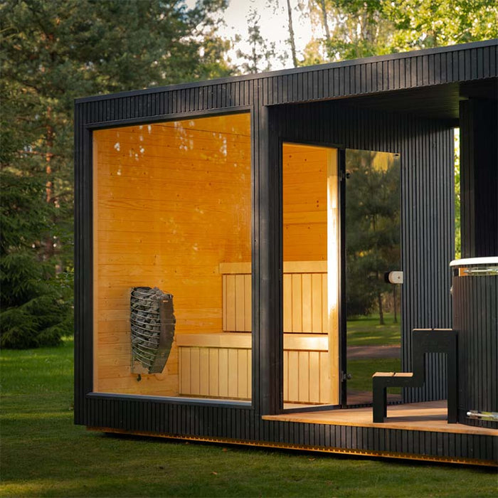 Corner angle of the Tauras Classic 7-person sauna highlighting the clear glass walls and spacious hot tub area, perfectly integrated into an outdoor landscape.