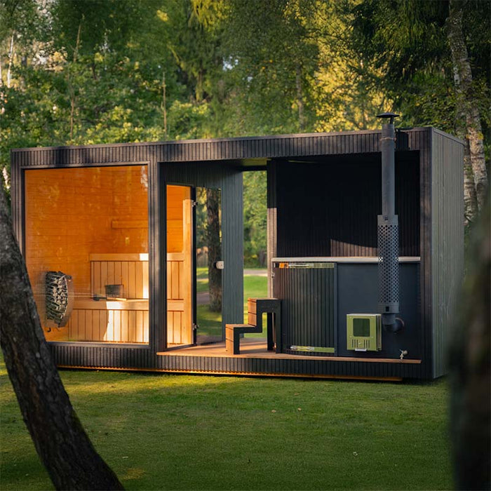 Full side view of the Tauras Classic 7-person sauna and hot tub cabin in a garden setting, blending natural wood interiors with modern black exterior.