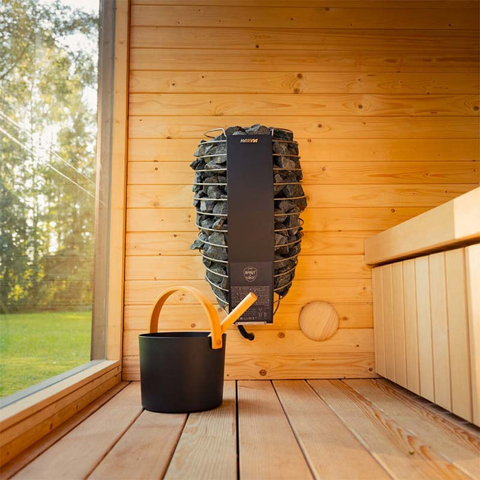 Interior view of the Tauras Classic sauna showing the Harvia stone heater, wooden bucket, and bench seating, designed for luxury 7-person sauna sessions.