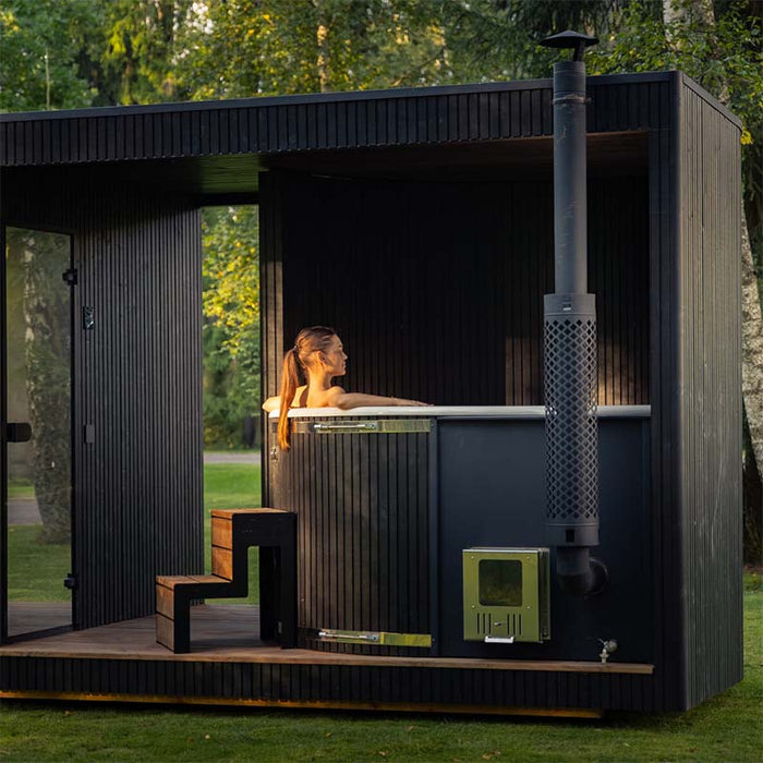 Woman relaxing in the built-in outdoor hot tub of the Tauras Classic 7-person sauna, enjoying a tranquil moment in nature with spa-like comfort.