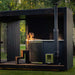 Woman relaxing in the built-in outdoor hot tub of the Tauras Classic 7-person sauna, enjoying a tranquil moment in nature with spa-like comfort.