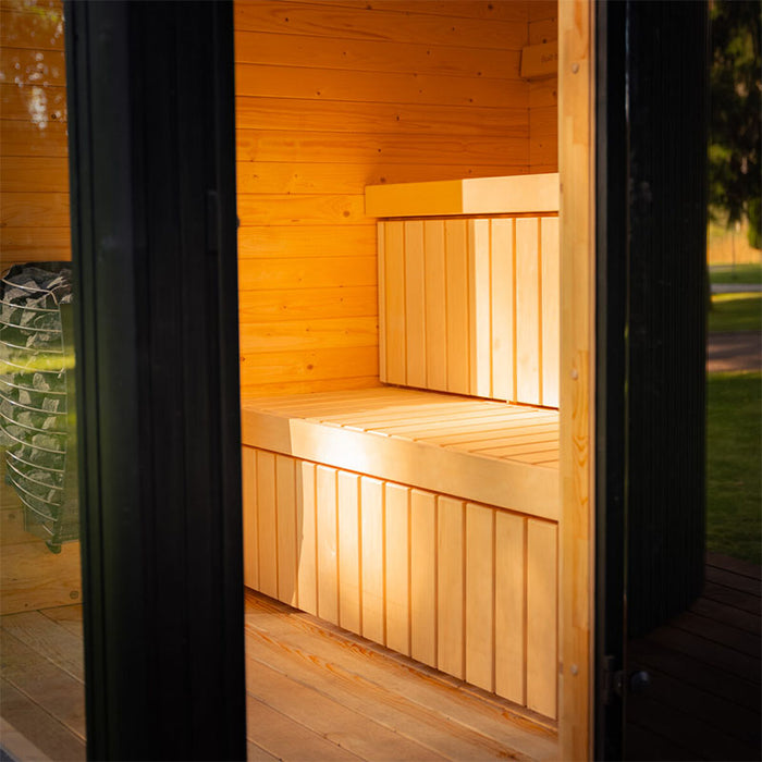 Warm and inviting entrance into the Tauras Classic sauna with glass door and soft lighting, showing wooden benches and Harvia heater inside.