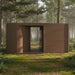 Nature-inspired brown Tauras Modular Air 7-person sauna cabin in a peaceful woodland setting, blending modern design with forest tranquillity for a calming sauna escape.