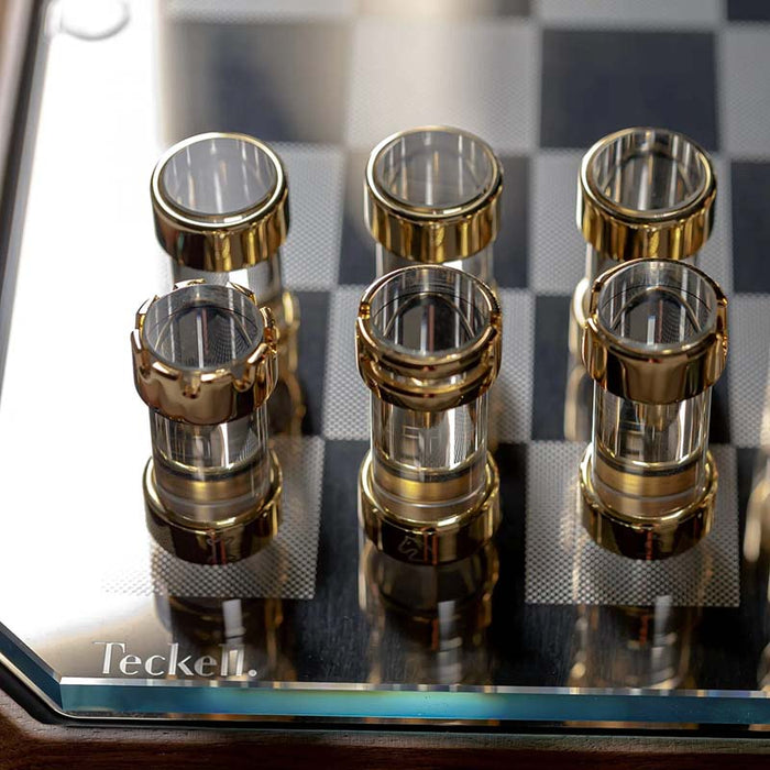 A close-up view of the meticulously crafted chess pieces, showcasing their intricate design with 24K gold and chrome-plated brass on extra-clear borosilicate glass cylinders.