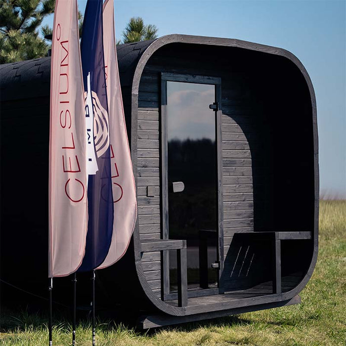 Angled exterior view of the Ula Grand 6-person outdoor sauna in ebony finish with flags and outdoor setting.