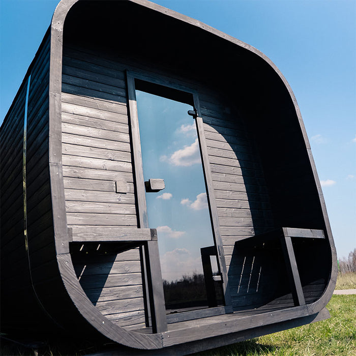 Angled front view of the Ula Grand 6-Person Outdoor Sauna in Ebony finish with glass door and outdoor seating.