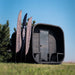 Wide outdoor view of the Ula Grand 6-person outdoor sauna in ebony finish with branded flags beside it.