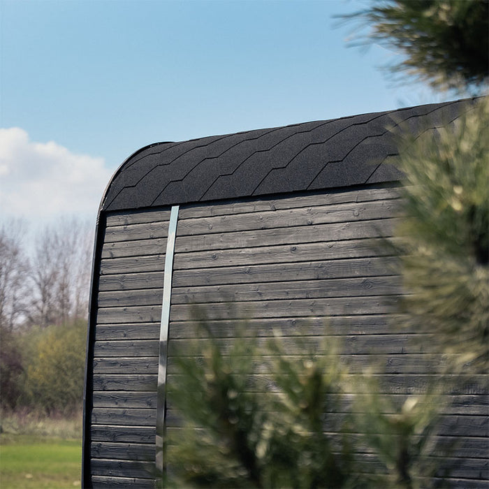 Wide outdoor shot of the Ula Grand 6-Person Outdoor Sauna in Ebony finish placed on grass with branding flags