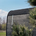 Wide outdoor shot of the Ula Grand 6-Person Outdoor Sauna in Ebony finish placed on grass with branding flags