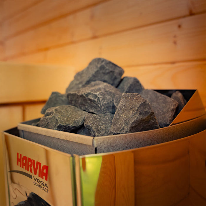 Detailed close-up of Harvia Vega Compact heater stones inside the Ula Micro 2-person outdoor sauna, highlighting the natural rock texture and warm wooden interior.