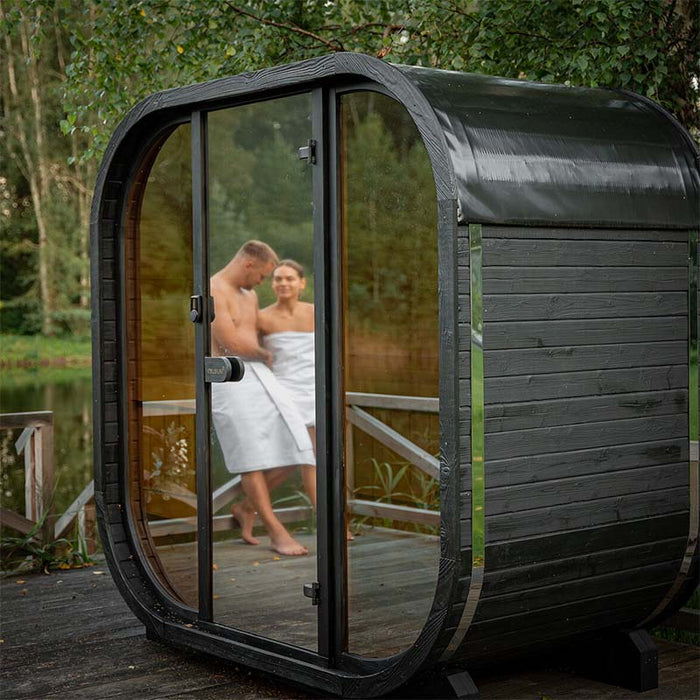 Exterior front view of the black Ula Mini outdoor sauna with couple visible through the glass door.