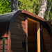Angled side view of the Ula Mini sauna showing curved roof and smooth timber panelling against lush greenery.