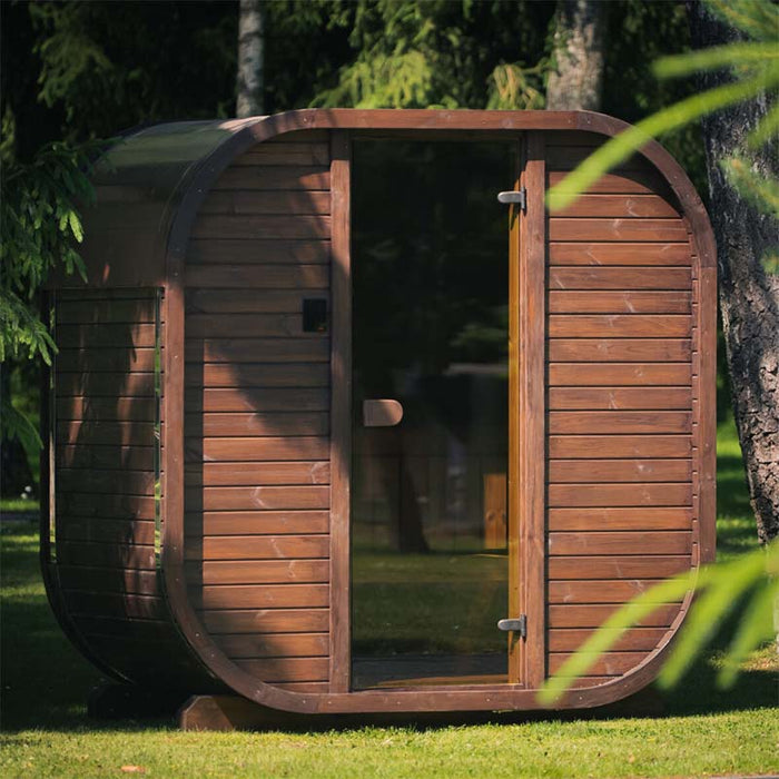 Ula Mini 2-person outdoor sauna with a rounded wooden exterior, positioned in a tranquil garden surrounded by trees.
