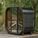 Couple walking towards the Ula Mini 2-person outdoor sauna positioned by a serene lakeside deck.