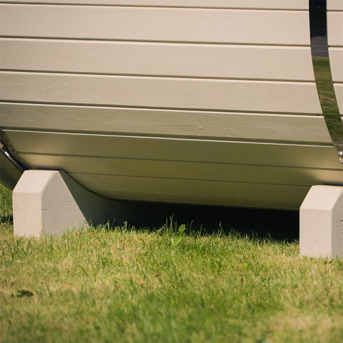 Close-up of the base support structure of a white Ula Mini sauna, resting on green grass.