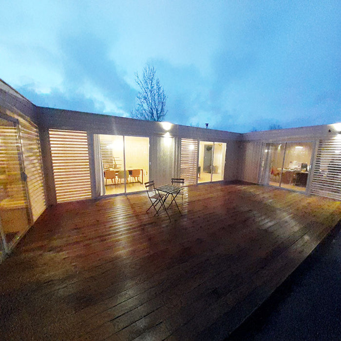 Illuminated Glamping Cube 51m² U-Shape model showcasing wooden exterior and warm interior lighting at dusk.