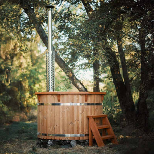 A 1.9m thermowood hot tub with a tall chimney and wooden steps, set in a tranquil woodland setting.