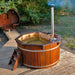 A 1.9m thermowood hot tub on a wooden deck next to a cabin, featuring a chimney and wooden steps.