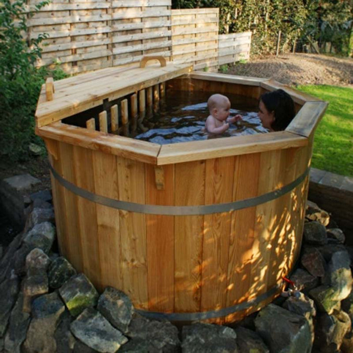 A mother and child enjoying a 1.9m thermowood hot tub in a garden with a wooden fence.