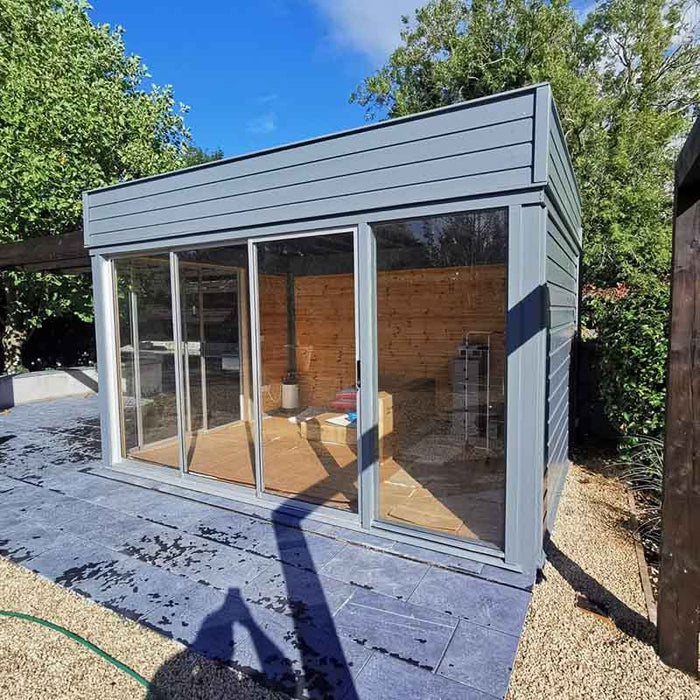 Modern grey Insulated Garden Office Cube 3 x 4m with sliding glass doors, blending seamlessly into an outdoor setting on a tiled patio.