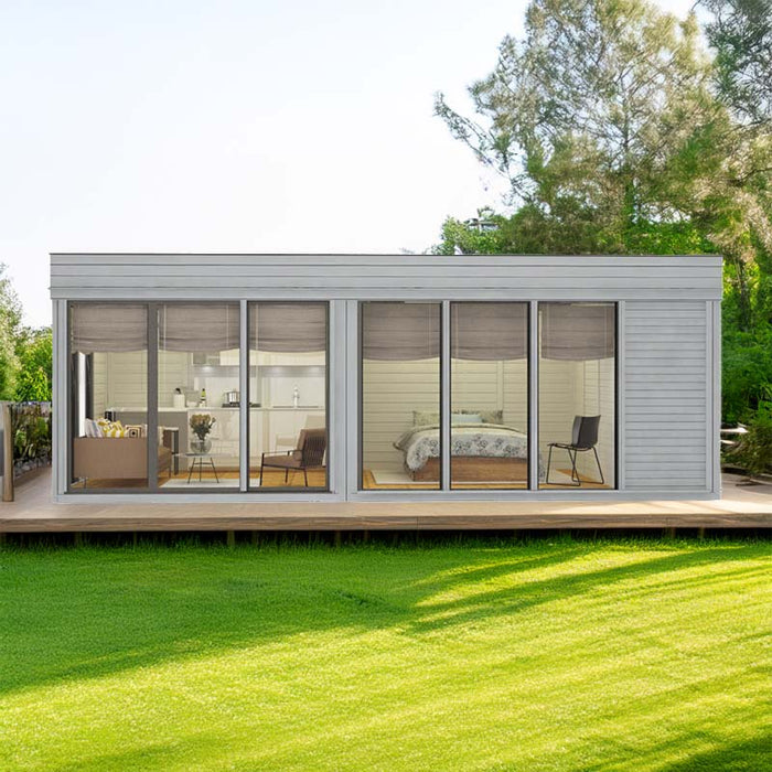 Insulated Glamping Cube 3 x 7m in a lush garden setting, featuring large glass panels that reveal a cosy, modern interior with separate living and bedroom areas, ideal for year-round outdoor relaxation.