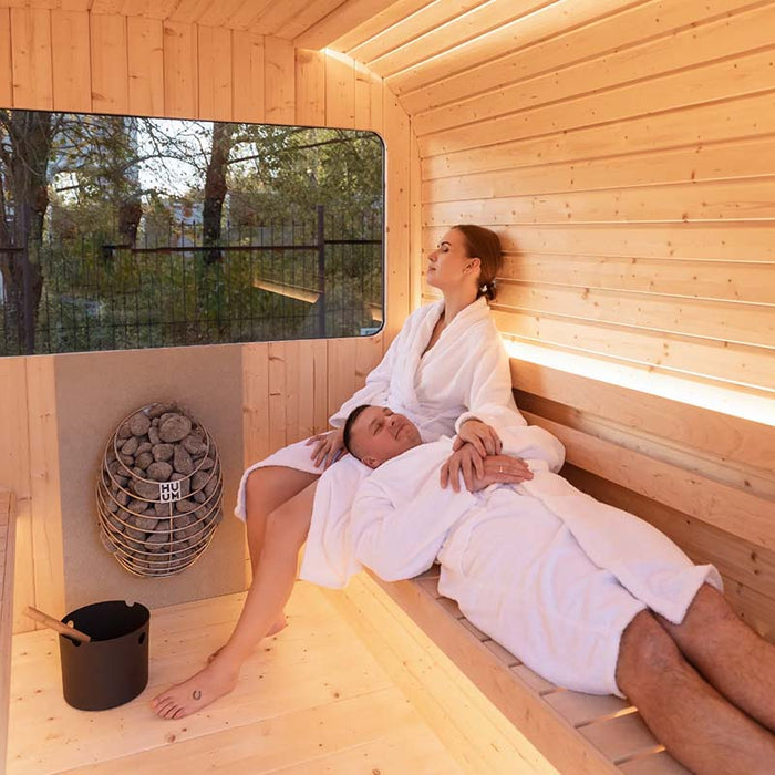 Relaxing couple in Luna Outdoor Sauna 2.3 x 2.4m with HUUM heater, bucket and ladle.